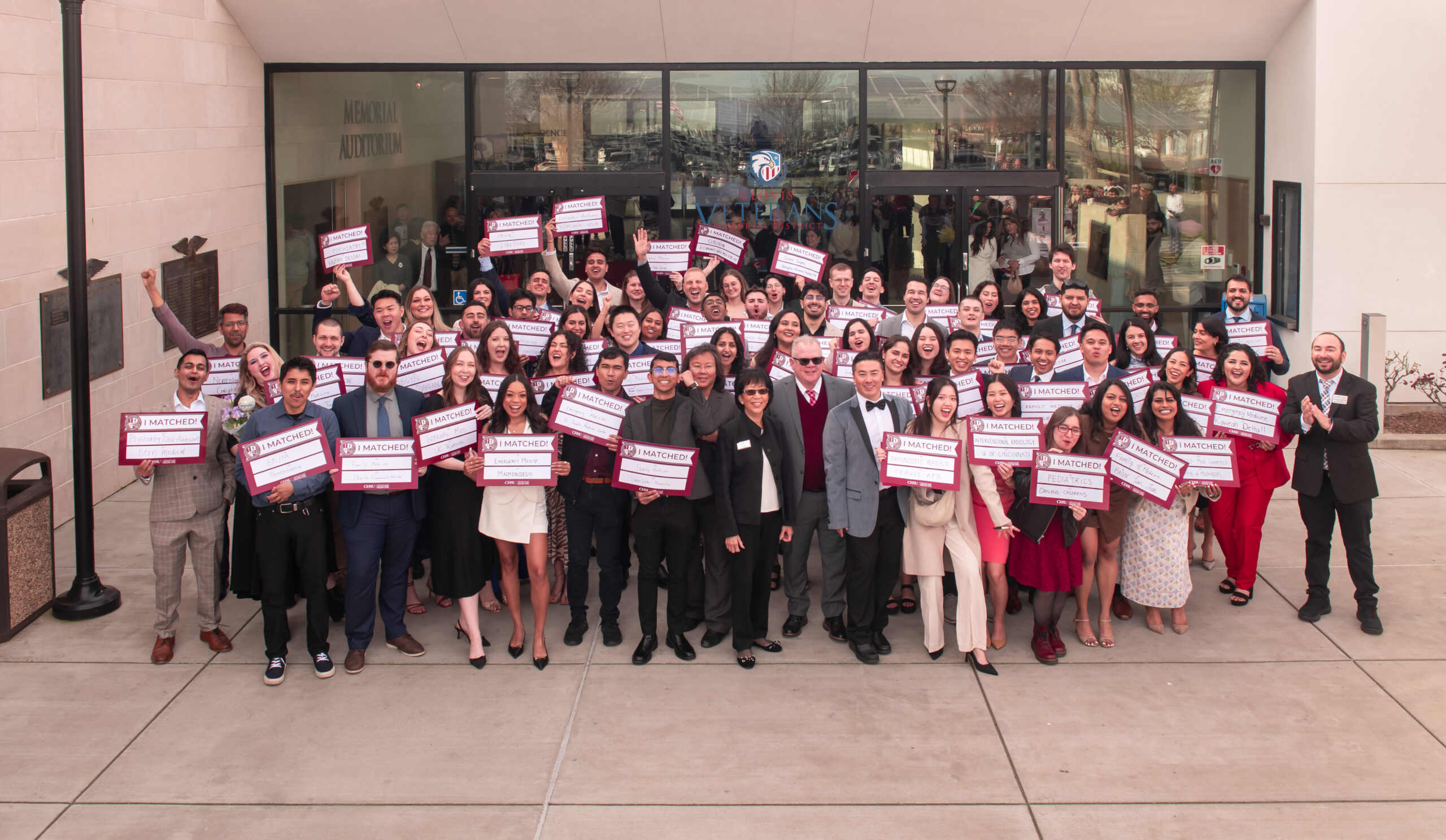 Group photo of students holding I Matched signs with faculty and staff in front of building