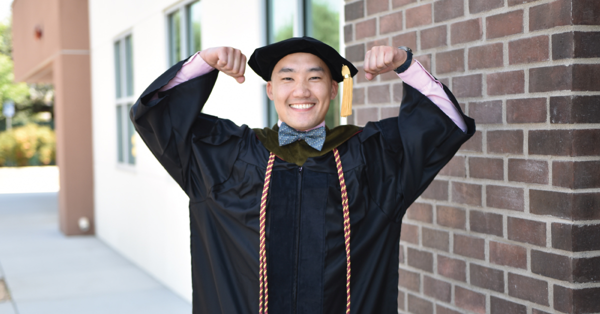 Man in graduation regalia flexing arms