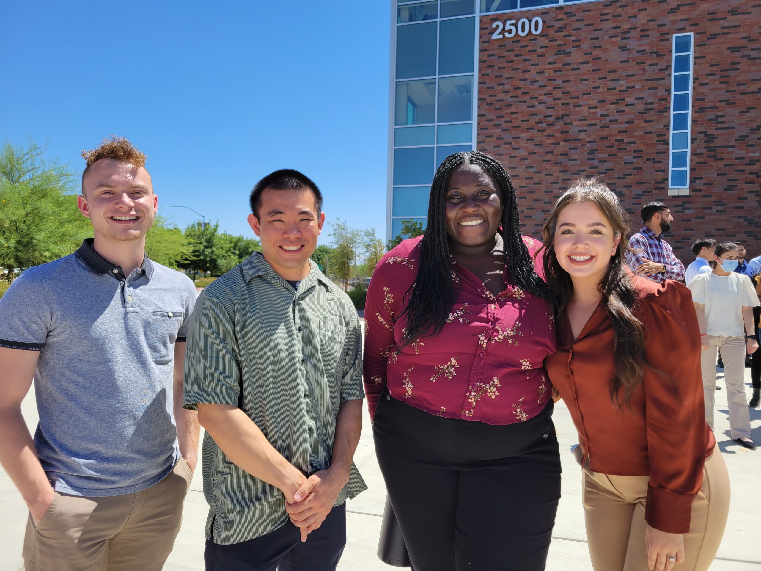 Four people in group photo in front of building