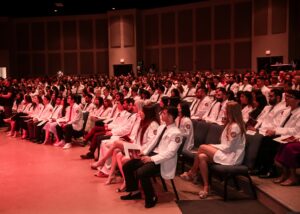 Students wearing white coats seated in auditorium