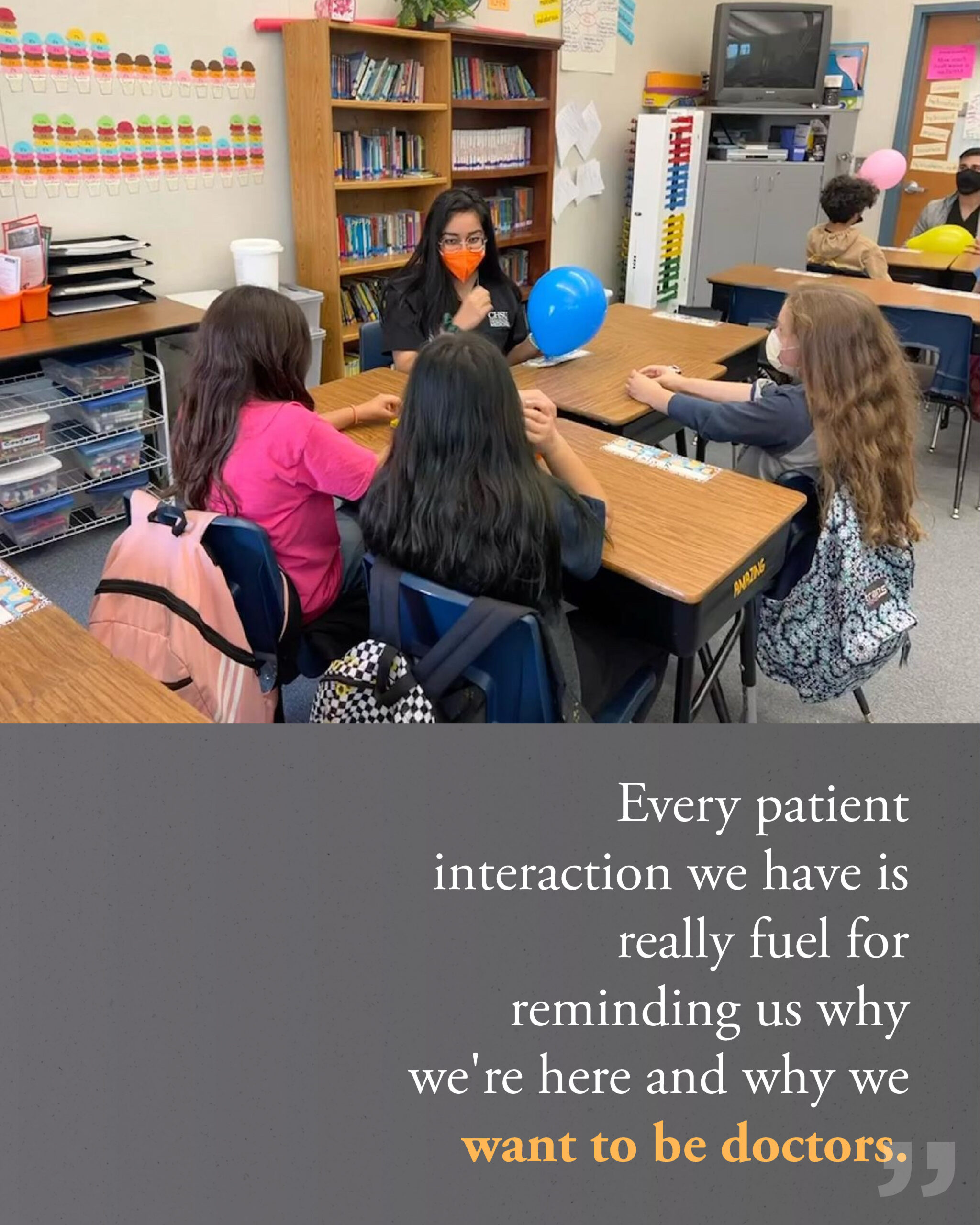 medical student wearing face mask holding balloon and talking to 3 elementary students in library