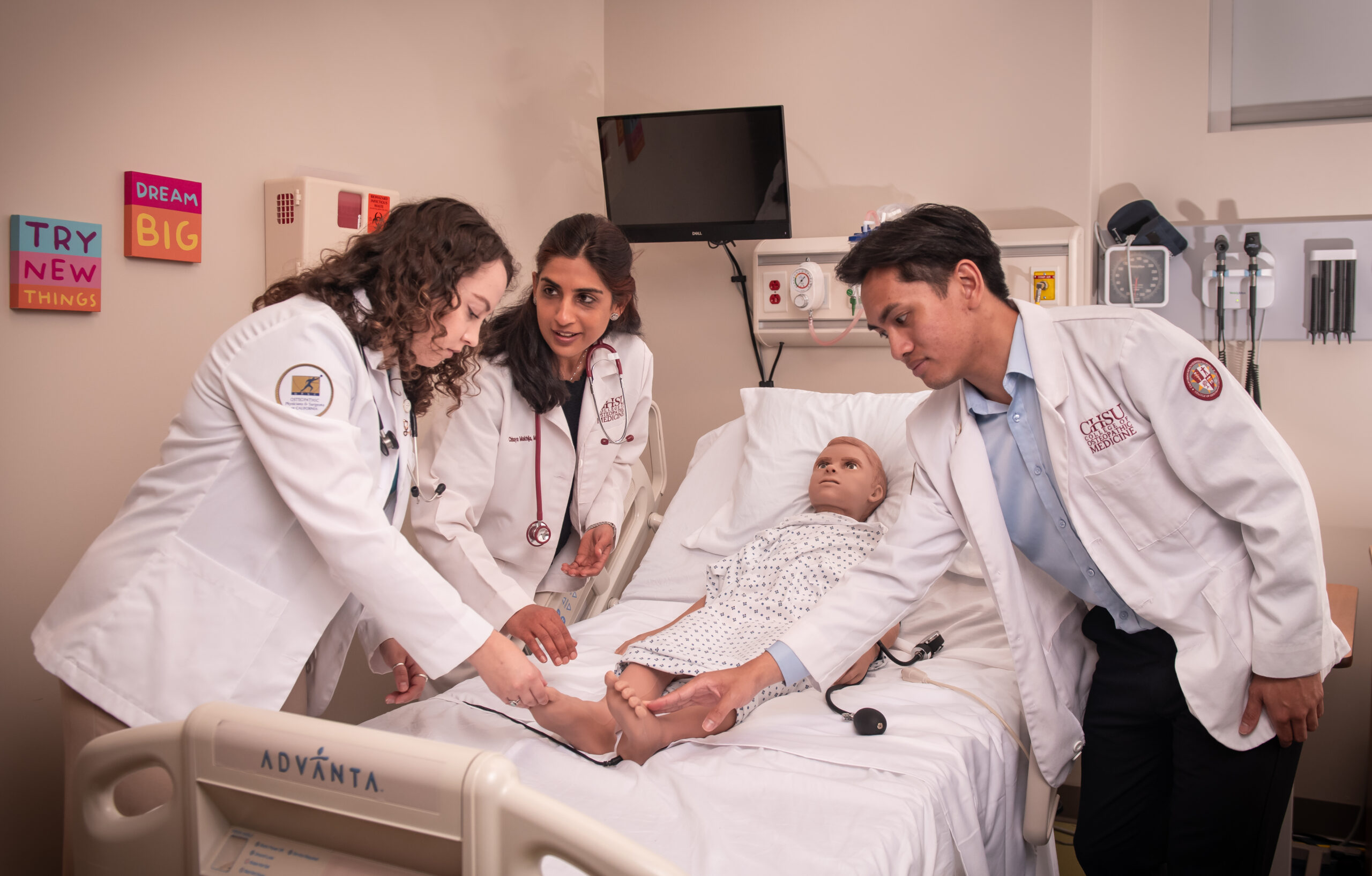 physician faculty teaching two medical students in simulated hospital room with pediatric manikin