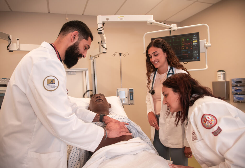 3 people simulating exam on manikin in hospital bed