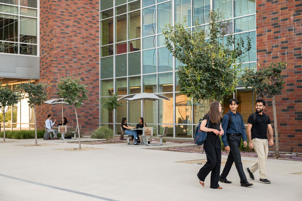 students seated at tables and students walking in COM courtyard