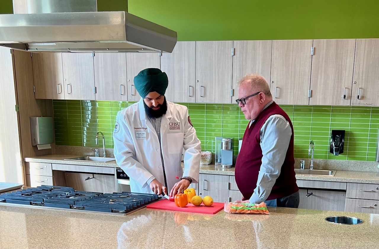 student chopping vegetables in teaching kitchen with dean watching