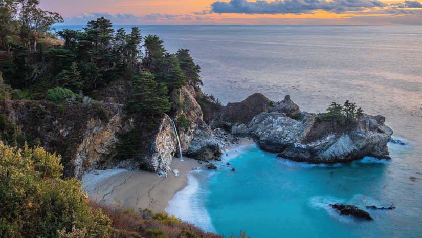 McWay Falls on California Central Coast with waterfall falling from granite rocks with trees, blue ocean cove, Pacific Ocean in background