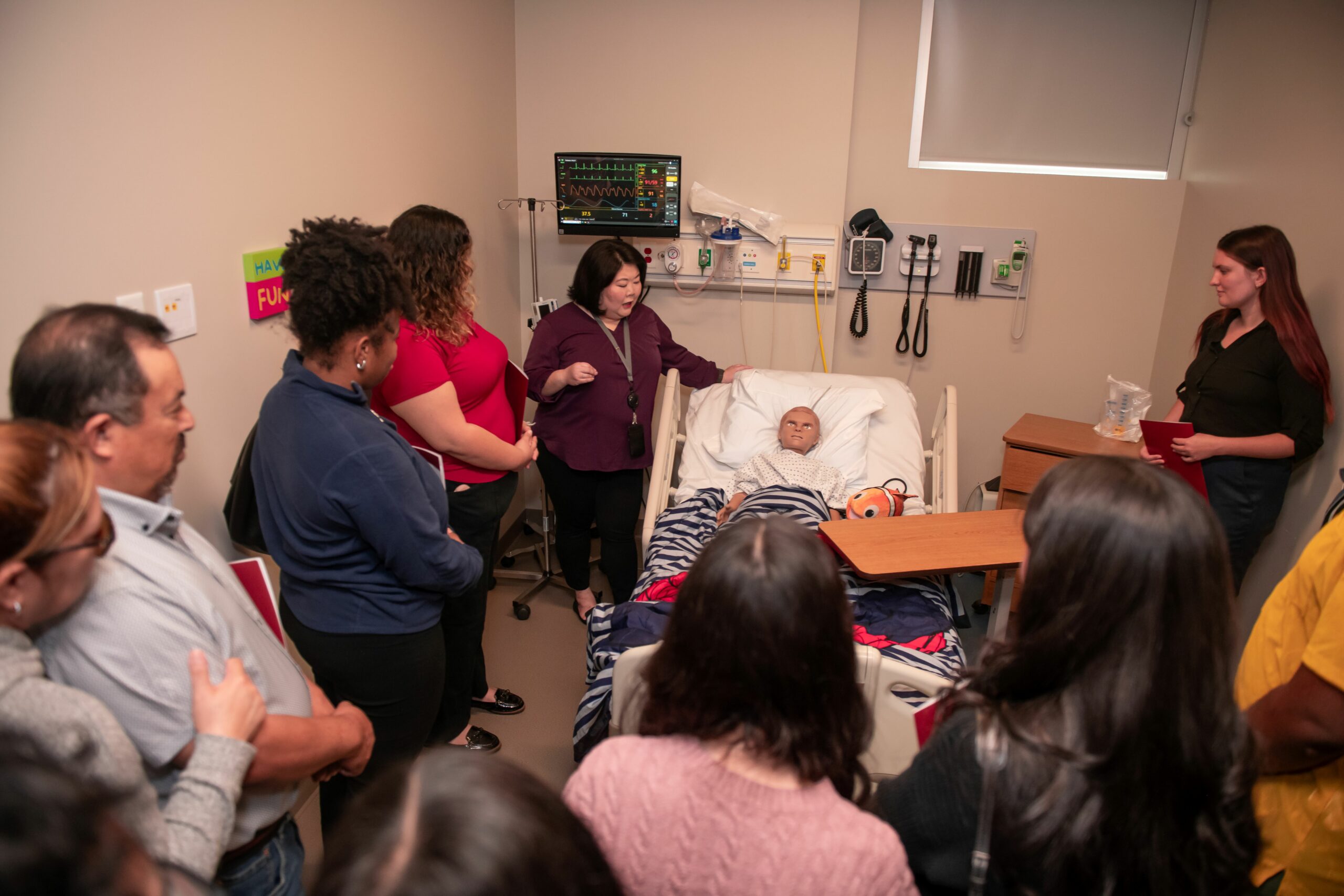 Simulated hospital room with child maniken in bed and group gathered around