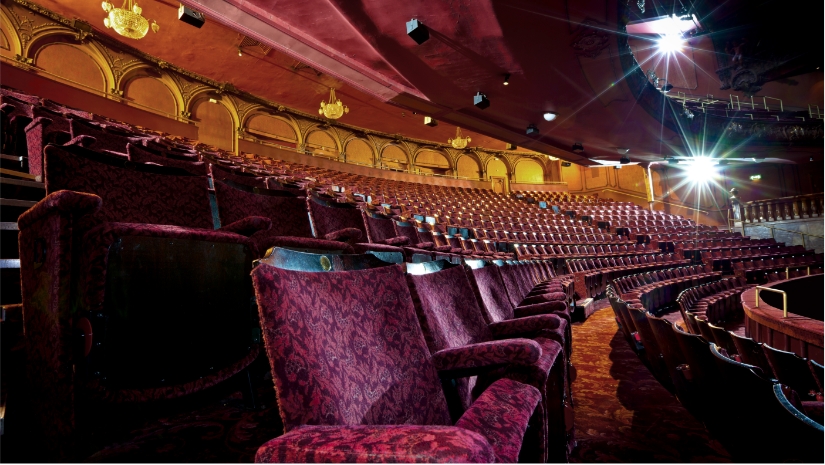 historic theater with maroon velvet theater seats with arched backwall and chandeliers